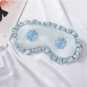 Primer plano de antifaz de seda azul con volantes y bordado floral para un sueño cómodo.