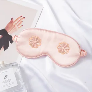 Close-up of pink silk sleep eye mask with delicate 3D floral embroidery and soft elastic band.