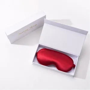 Close-up detail of smooth red silk eye mask inside white gift box packaging, soft fabric.