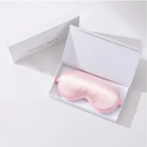 Detail shot of a pink silk eye mask inside a luxury white gift box with soft lighting.