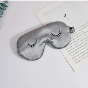 Detailaufnahme einer grauen Seidenschlafmaske mit süßer Wimpernbestickung für die Nachtruhe.