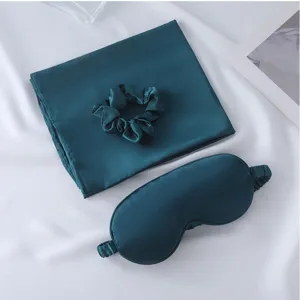 Silk satin sleep set detail showing smooth teal pillowcase, mask and scrunchie texture.