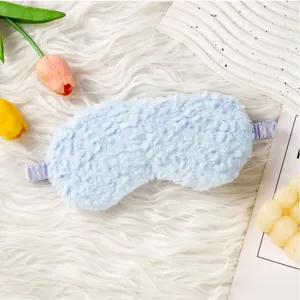 Primo piano dettaglio di maschera da sonno in peluche azzurro con fascia elastica su tappeto bianco.