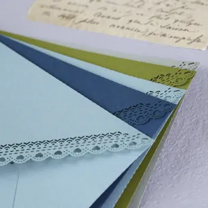 Laser cut lace detail on colored triangular envelopes, elegant wedding invitation close up.