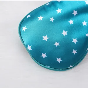 Close-up detail of teal silk sleep mask with white star print and soft trim edge.