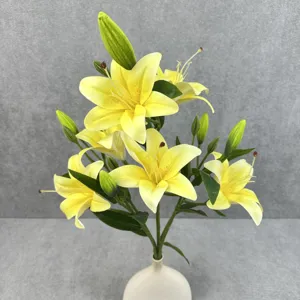 Detailed view of yellow artificial lily flower arrangement with green leaves in white vase.