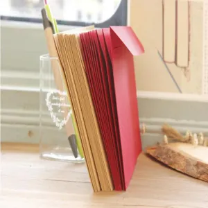 Kraft paper envelopes in red and brown colors, displayed in a clear holder with pens on a wooden desk.