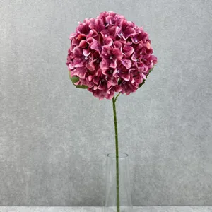 Artificial silk hydrangea flower stem detail with deep pink petals in a clear glass vase.
