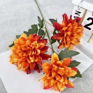Vue détaillée de fleurs artificielles de dahlias artificiels orange rouge avec de belles feuilles.