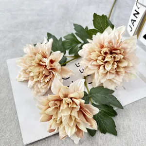 Vue détaillée de fleurs de dahlias artificielles champagne élégantes avec feuilles vertes.