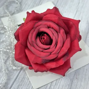 Close-up detail of a dark red artificial rose flower head with white backing card and beads decor.