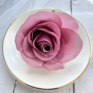 Detailed shot of dusty pink artificial rose flower head in white plate, floral accessory.