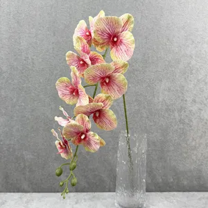 Gedetailleerde close-up van realistische kunstorchidee bloementak geplaatst in een heldere glazen vaas.