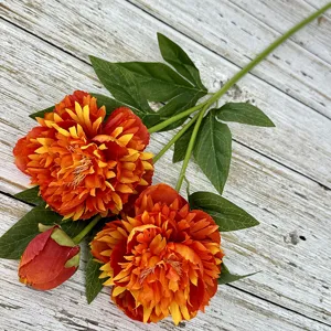 Close-up detail of artificial orange peony flower branch, showing realistic petals and green leaves.