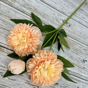 Detailed shot of artificial peony flower branch with blooms and buds on rustic wooden surface.