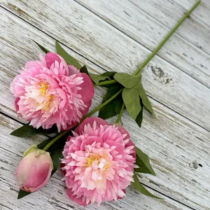 Detailed view of artificial pink peony flower stem with two blooms, bud and green leaves.