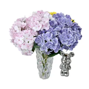 Artificial hydrangea flower bouquet in clear glass vase with silver bear decor for home.