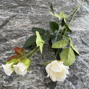 Vista ravvicinata dettagliata di un ramo di rosa artificiale con tre teste di fiori e foglie verdi.