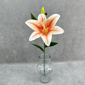 Close-up detail of artificial lily flower with realistic petals and green leaves in clear glass vase.