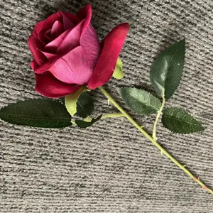 Vue détaillée d'une rose artificielle en velours avec feuilles vertes et tige réaliste.