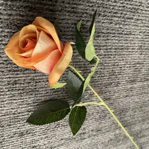Détail en gros plan d'une rose artificielle orange avec des feuilles vertes, décor floral faux.