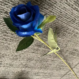 Gros plan détaillé d'une rose bleue artificielle avec des pétales vibrants, des feuilles et une tige.