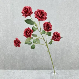 Vue détaillée de roses rouges artificielles à 6 têtes avec feuilles dans un vase en verre.