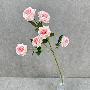 Gros plan d'une branche de roses artificielles roses avec feuilles vertes dans un vase.