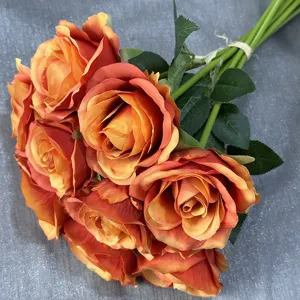 Nahaufnahme eines künstlichen orangefarbenen Rosenstraußes mit grünen Blättern und Stielen.