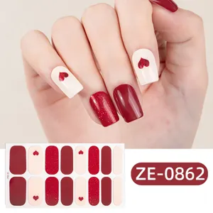 Close-up of red glitter and heart nail polish wrap stickers detail on hand model.