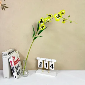 Artificial yellow orchid flower branch with glass vase, elegant home decor table arrangement.