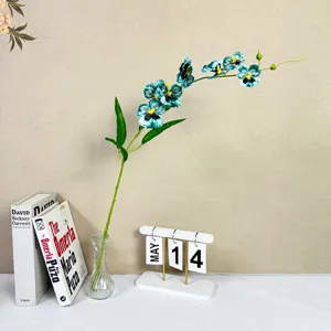 Detail shot of artificial blue orchid flower arrangement with glass vase and decorative books.