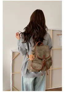 Detail shot of casual canvas backpack with brown leather trim and cute bear charm in studio setting.