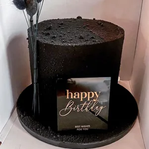 Detailed view of black velvet birthday cake with acrylic happy birthday topper and dark dried floral