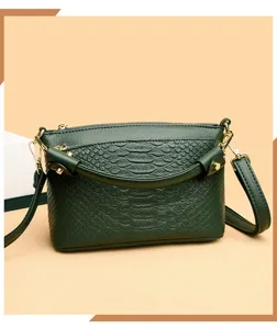 Close-up detail of dark green crocodile pattern leather crossbody handbag with gold hardware.