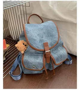 Denim backpack detail showcasing brown leather trim, dual pockets, and cute bear plush charm.