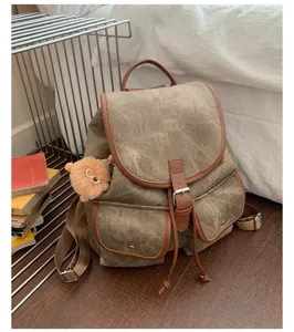 Vintage canvas backpack detail showing retro brown leather trim, front buckle flap and side charm.
