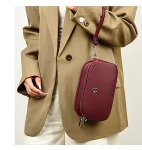 Detail view of dark red pebbled leather phone clutch bag with wrist strap and silver logo.
