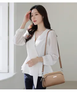 Detail view of stylish textured leather shoulder bag with metal accent and elegant white outfit.