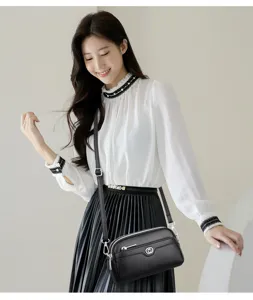 Black leather crossbody bag detail view featuring silver tone hardware and double zip design.