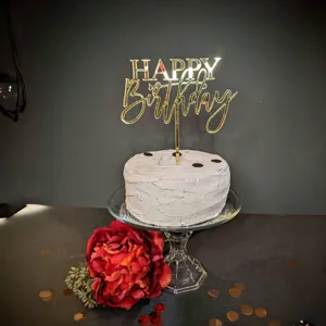 Detailansicht des goldenen Acryl Happy Birthday Kuchettoppers mit roter Blumendekoration.