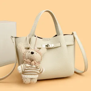 Cream leather women handbag with metal lock and cute plush bear charm for daily use.