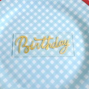 Clear acrylic birthday cake topper with gold cursive text, perfect party decoration detail.