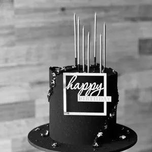 Minimalist black birthday cake with acrylic happy birthday topper and elegant tall candles.