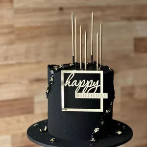 Black birthday cake detail showcasing gold candles and modern acrylic happy birthday topper.