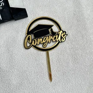 Black and gold graduation acrylic cake topper with Congrats lettering for party decor.
