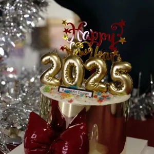 Close-up of 2025 New Year cake topper, gold number candles and red acrylic decoration.