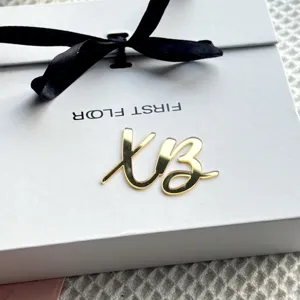 Close-up detail of gold mirror acrylic script ornament on white gift box with black ribbon.