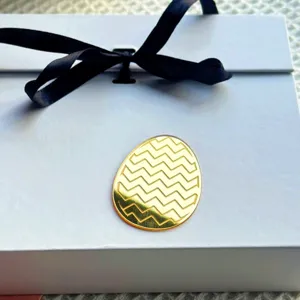 Close-up of a gold acrylic Easter egg charm with a stylish zigzag pattern on a gift box.