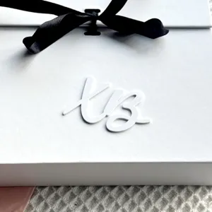 White gift box with black ribbon and custom script letter decor for elegant packaging.